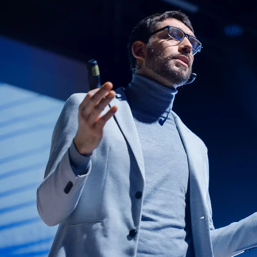 Person in glasses giving speech, holding small microphone.