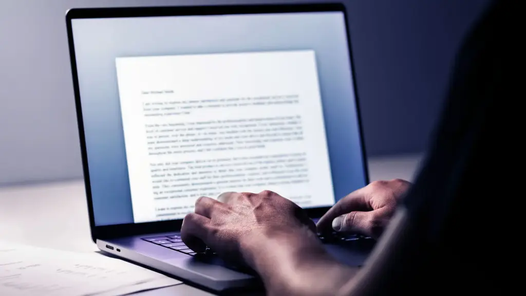 Person typing on a laptop, a word document.