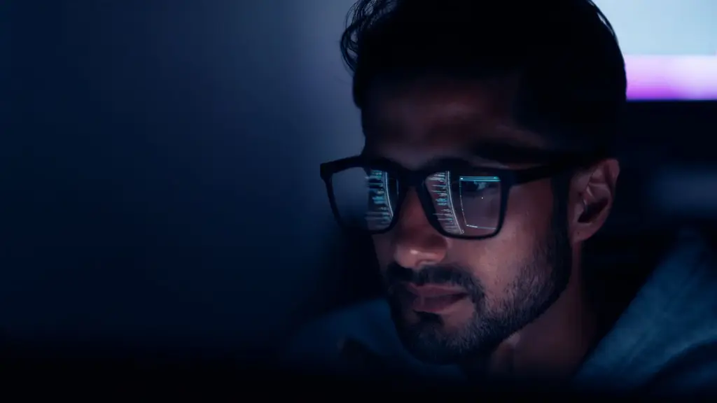 Man looking at screen with code seen in reflection of his glasses.