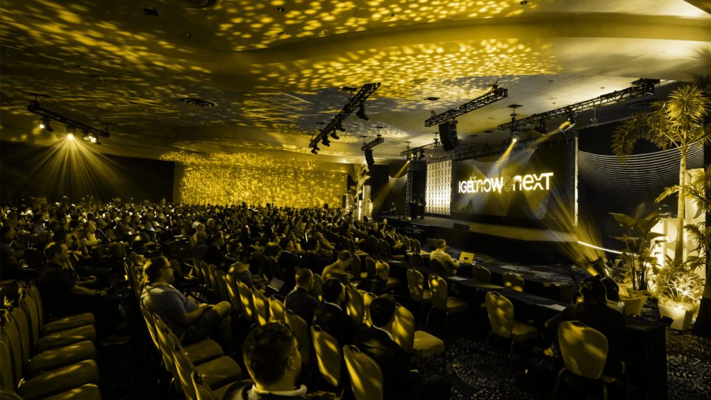 Yellow and black graded image of a crowd looking at the Now & Next branded screen.